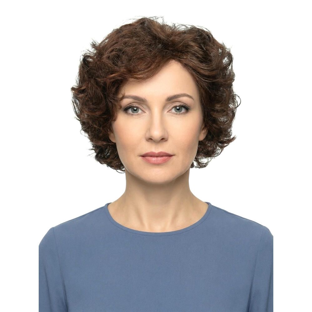 Frau mit brauner, lockiger Perücke. Frontansicht. Sie trägt ein blaues Oberteil. Hintergrund weiß.