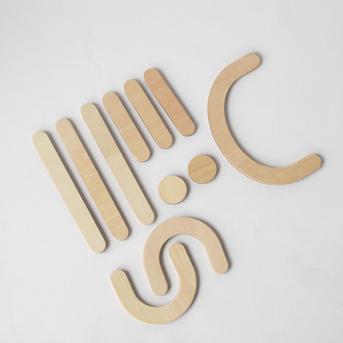 Holzbuchstaben und Formen. Einzelne Holzstücke in verschiedenen Formen. Zwei Kreise, zwei Bögen, mehrere gerade Stäbe.