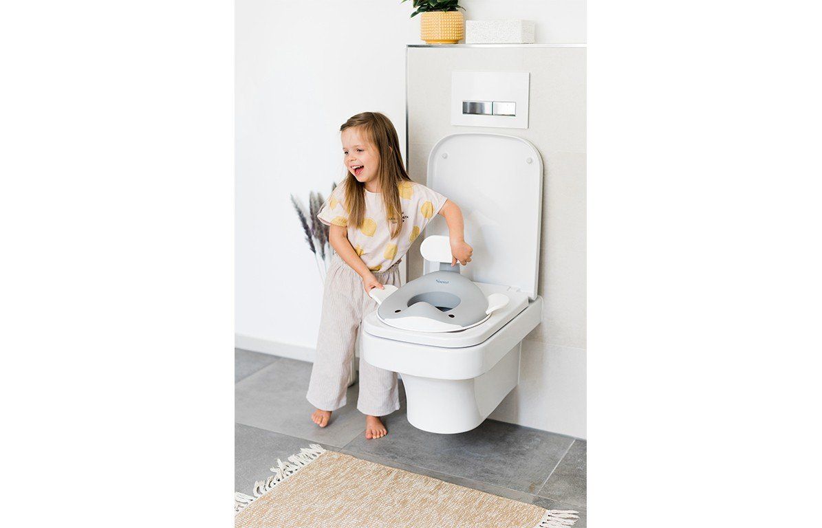 Kind hält den Toilettensitz in Walform. Kind steht vor Toilette. Badezimmer-Kontext.