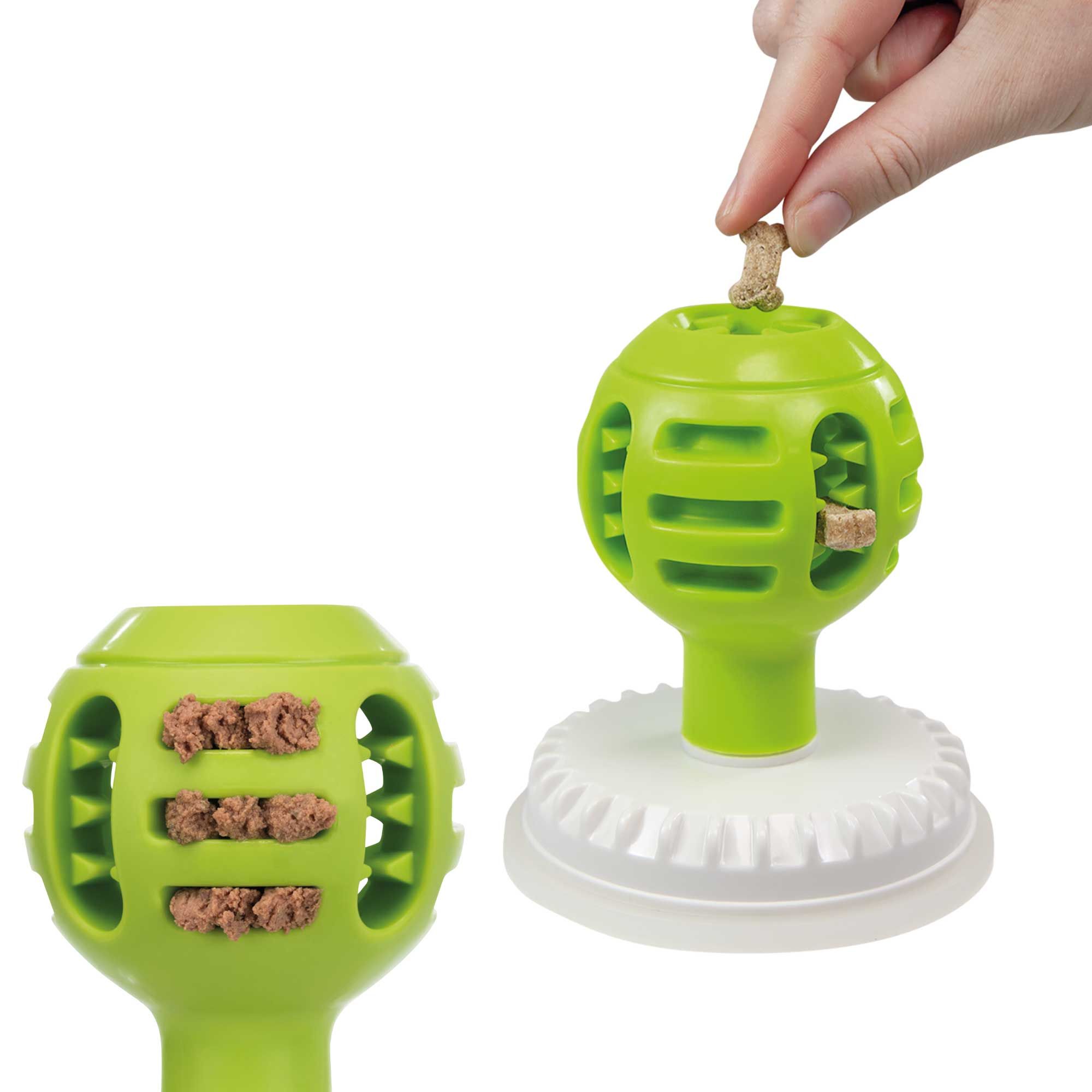 Zwei grüne Bälle mit Öffnungen und Füllung, auf weißer Basis. Eine Hand legt Futter in einen Ball.