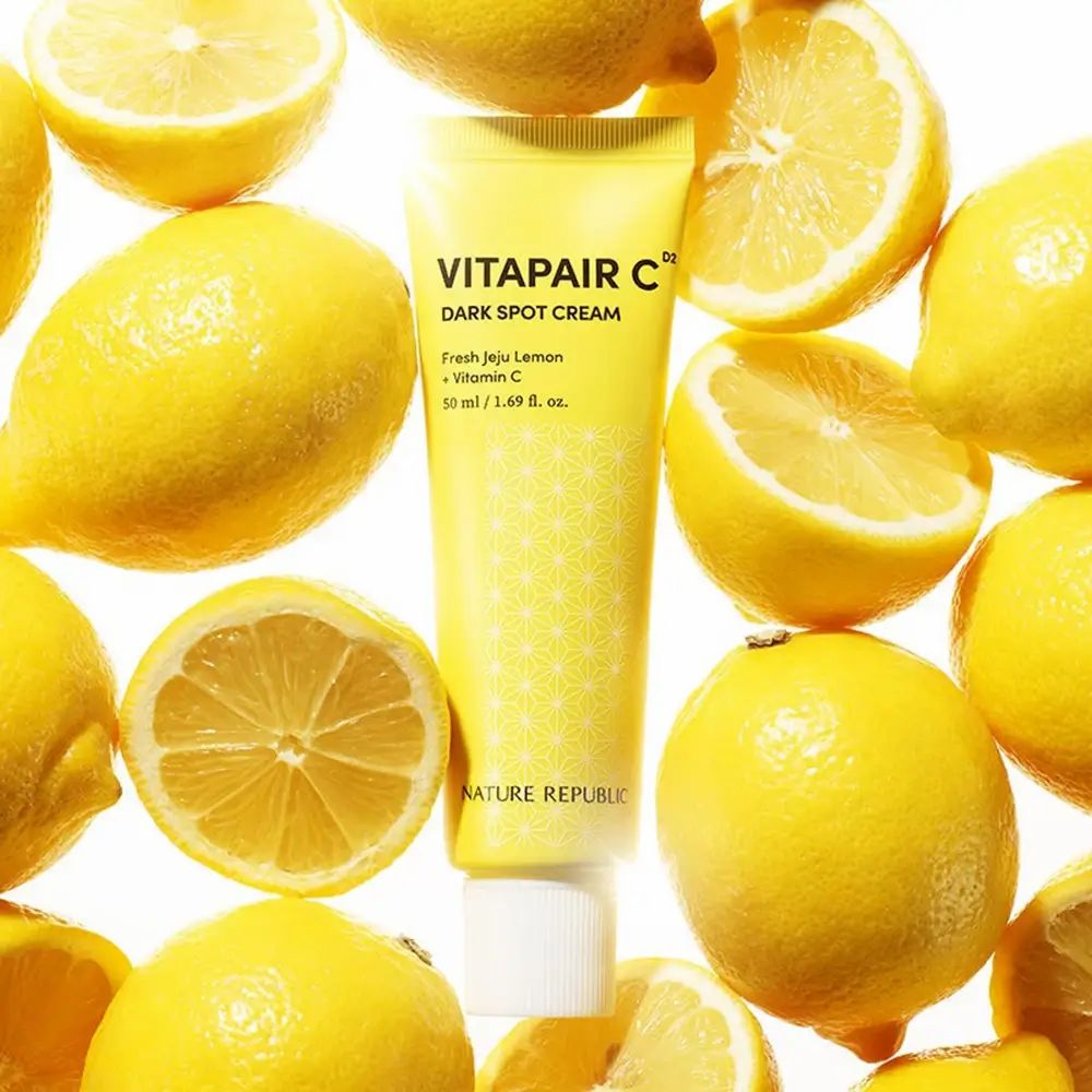 Eine gelbe Tube "Vitapair C Dark Spot Cream" umgeben von Zitronen. Die Tube ist von Zitronen umgeben.
