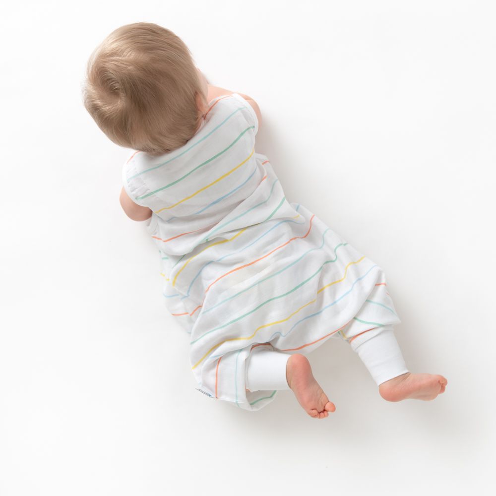 Draufsicht auf Baby im Schlafsack. Liegt auf dem Bauch, Blick nach oben. Weißer Hintergrund, helle Haut.