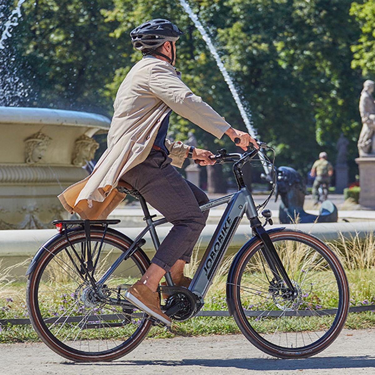 Person fährt ein graues E-Bike in einem Park. JOBOBIKE-Logo am Rahmen.