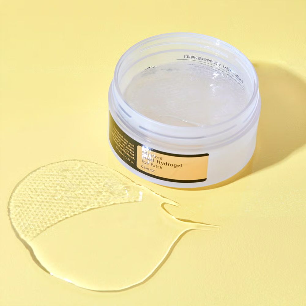 Ein offener Behälter mit Hydrogel-Augenpads und einem einzelnen Pad, das daneben liegt. Ein Spatel ist im Behälter sichtbar.
