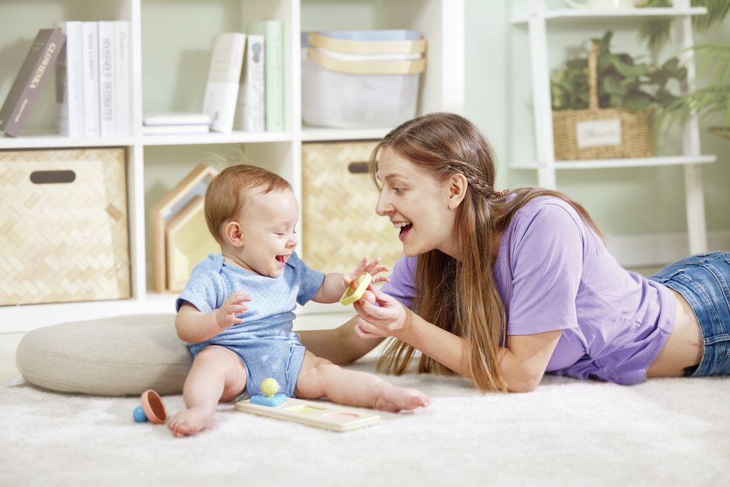 Baby und Frau spielen mit Holzpuzzle auf dem Boden. Puzzle mit farbigen Formen.
