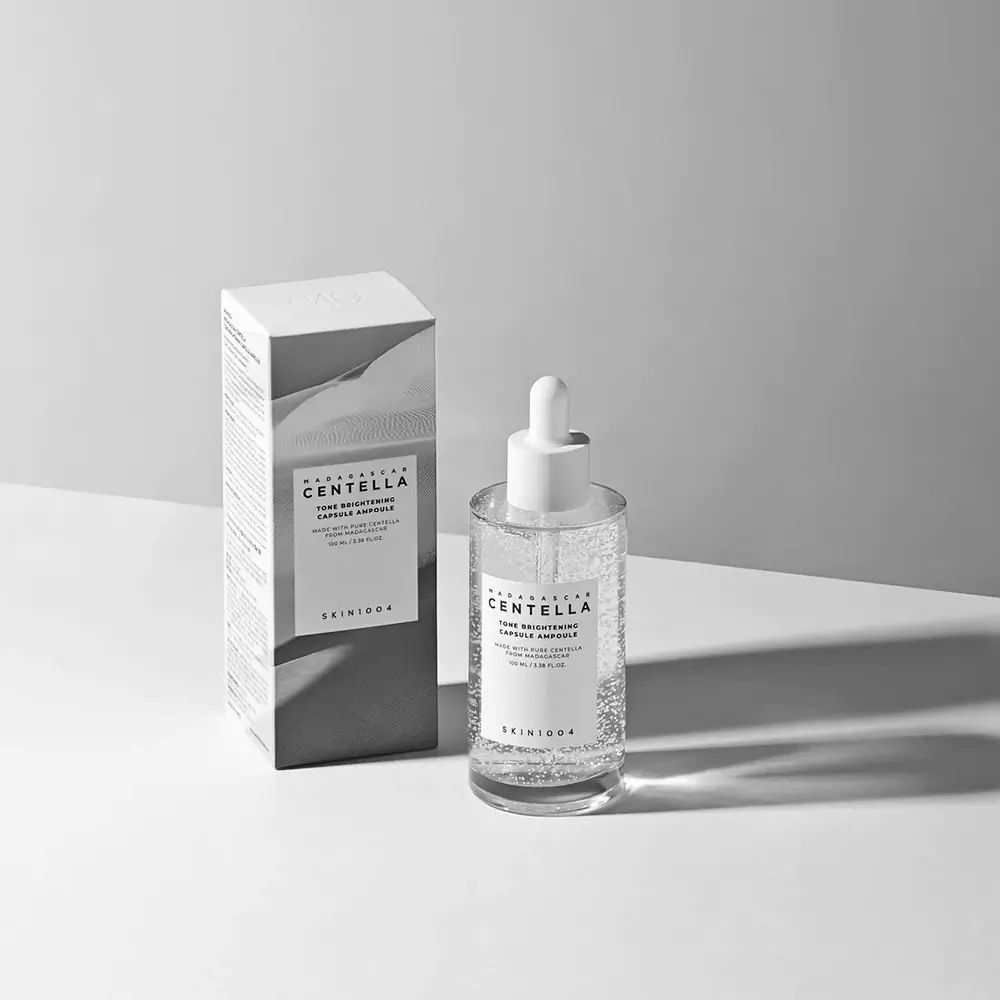 Produktflasche und Verpackung. Aufschrift: CENTELLA, TONE BRIGHTENING CAPSULE AMPOULE. SKIN1004-Logo.