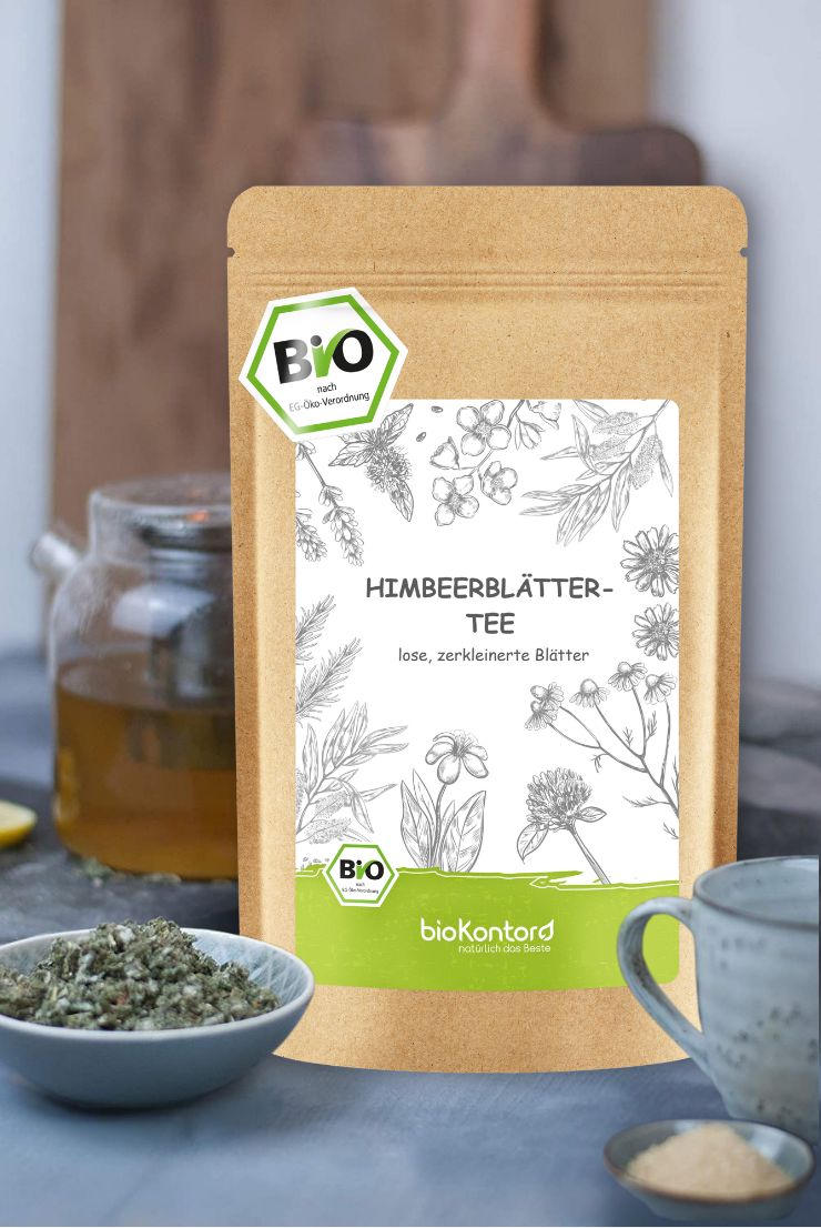 Braune Papierverpackung mit Himbeerblättertee-Etikett. Lose Blätter in Schale. Bio-Siegel. Hintergrund: Holzbrett, Teekanne, Tasse.