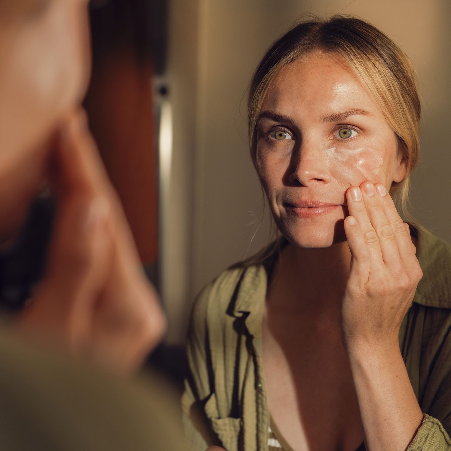 Frau trägt Creme auf. Spiegelbild. Hintergrund: Badezimmer.