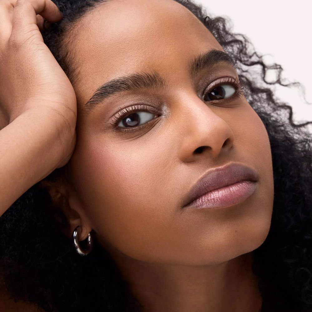 Nahaufnahme einer Frau mit rosafarbenem Lidschatten und Lippenstift. Sie stützt den Kopf auf ihre Hand.