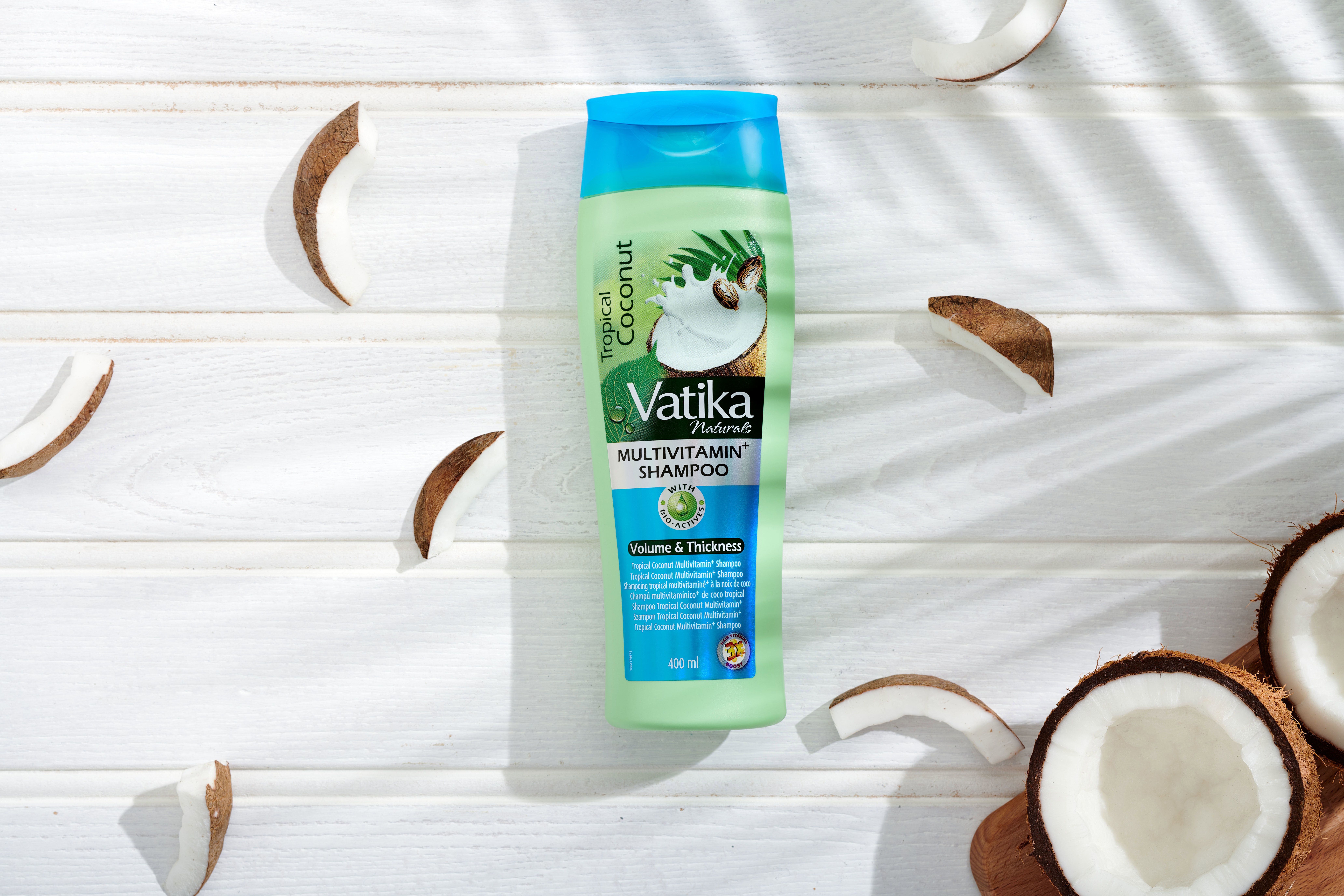 Grüne Shampoo-Flasche mit blauem Deckel, umgeben von Kokosnuss-Stücken. Aufschrift: Vatika Naturals Multivitamin Shampoo.