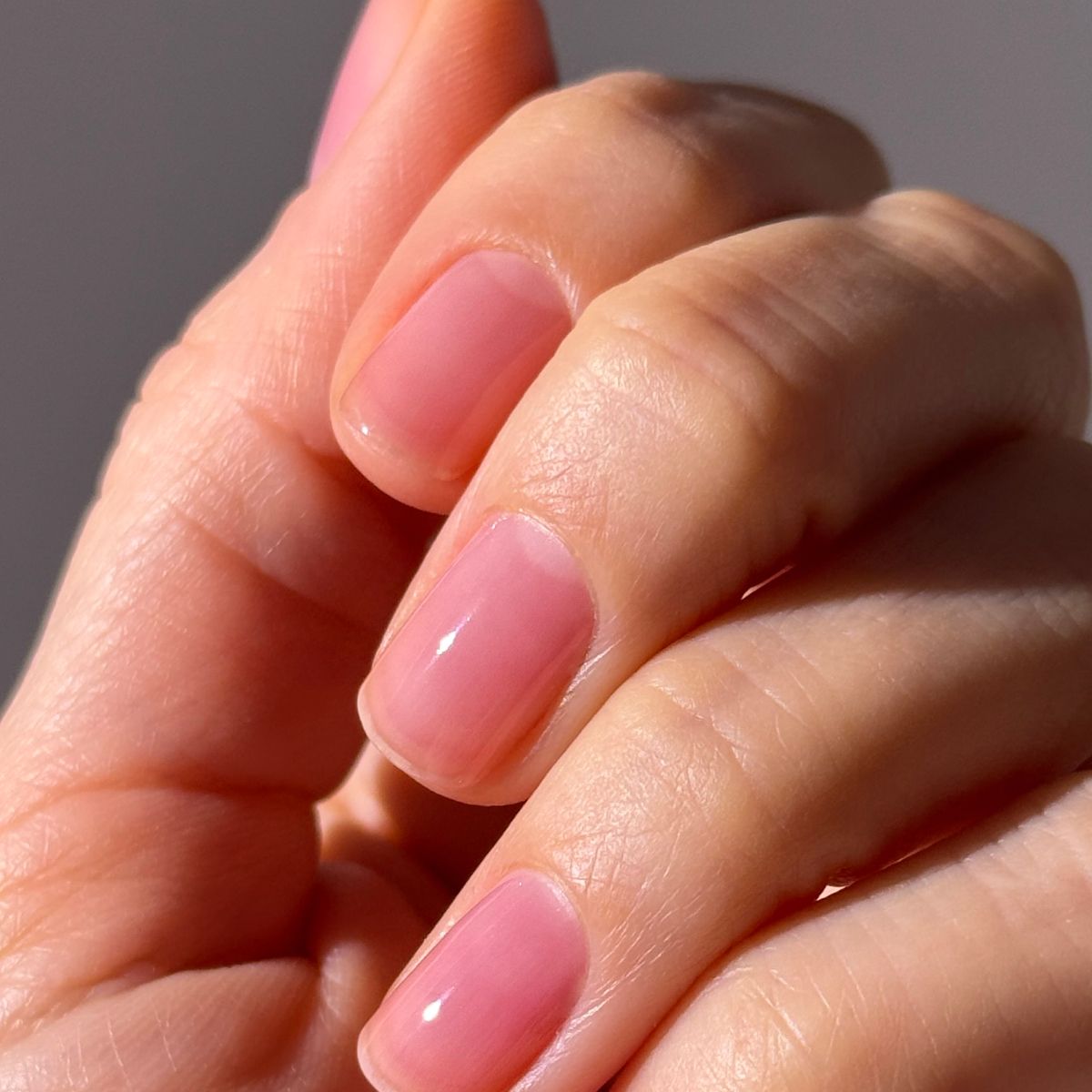 Nahaufnahme einer Hand mit kurz geschnittenen, rosa lackierten Nägeln.
