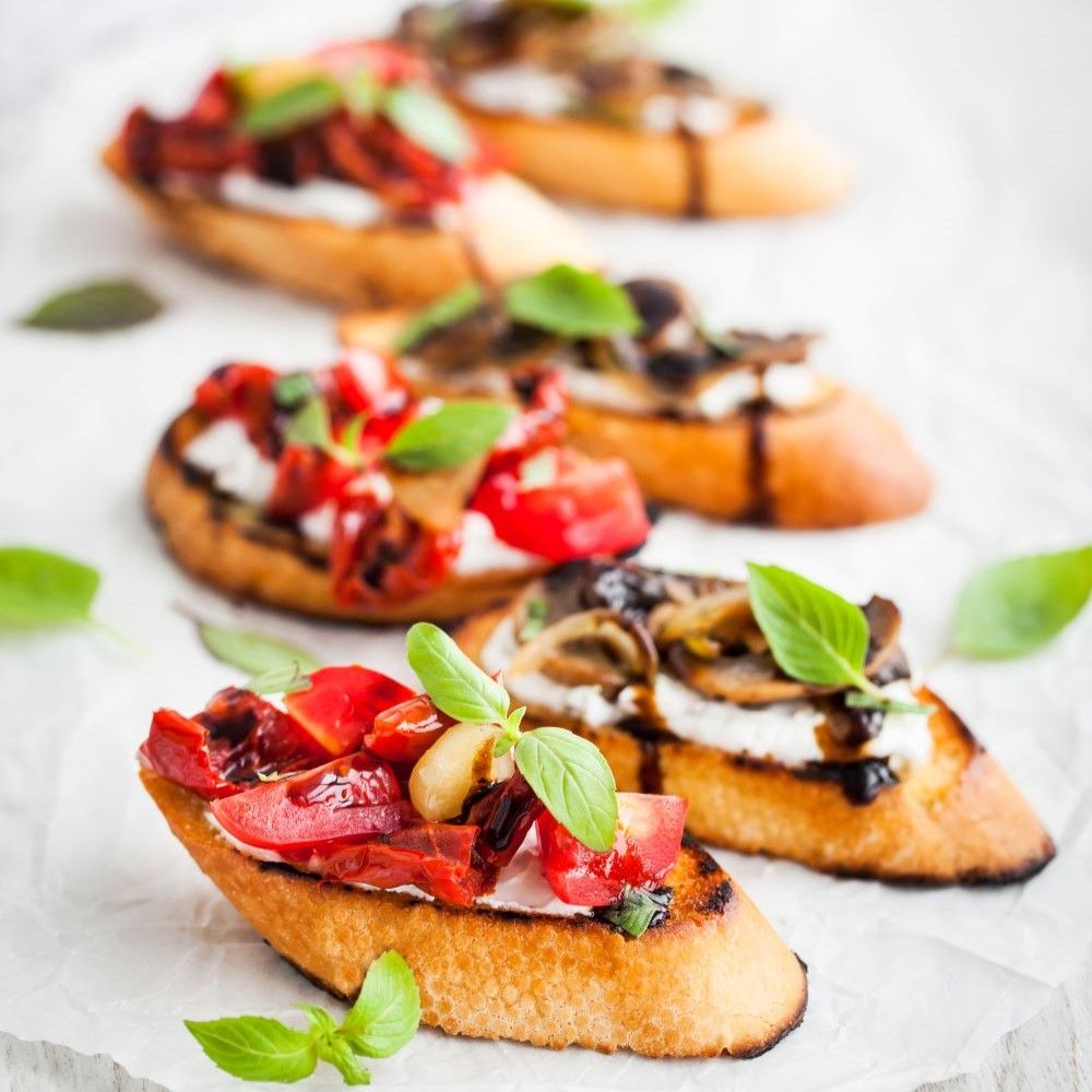 Bruschetta mit Tomaten, Pilzen und Basilikum. Brot mit Belag, arrangiert auf Papier.