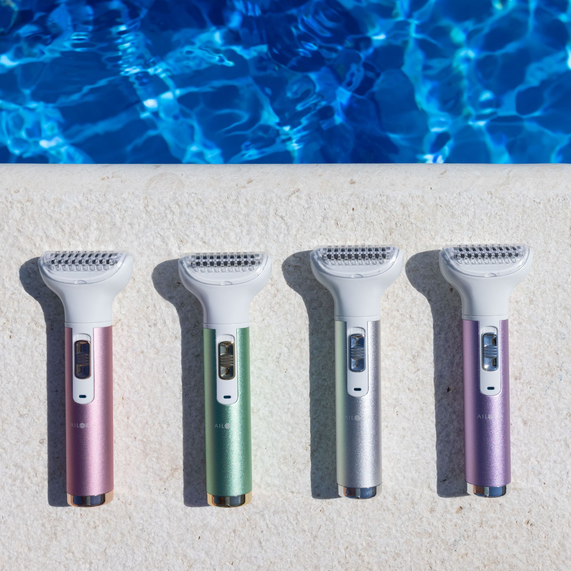 Vier Körperrasierer in verschiedenen Farben, neben einem Pool. Rosa, grün, silber und lila.
