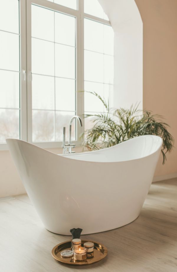 Freistehende Badewanne in hellem Badezimmer. Goldene Ablage mit Kerzen und Accessoires.