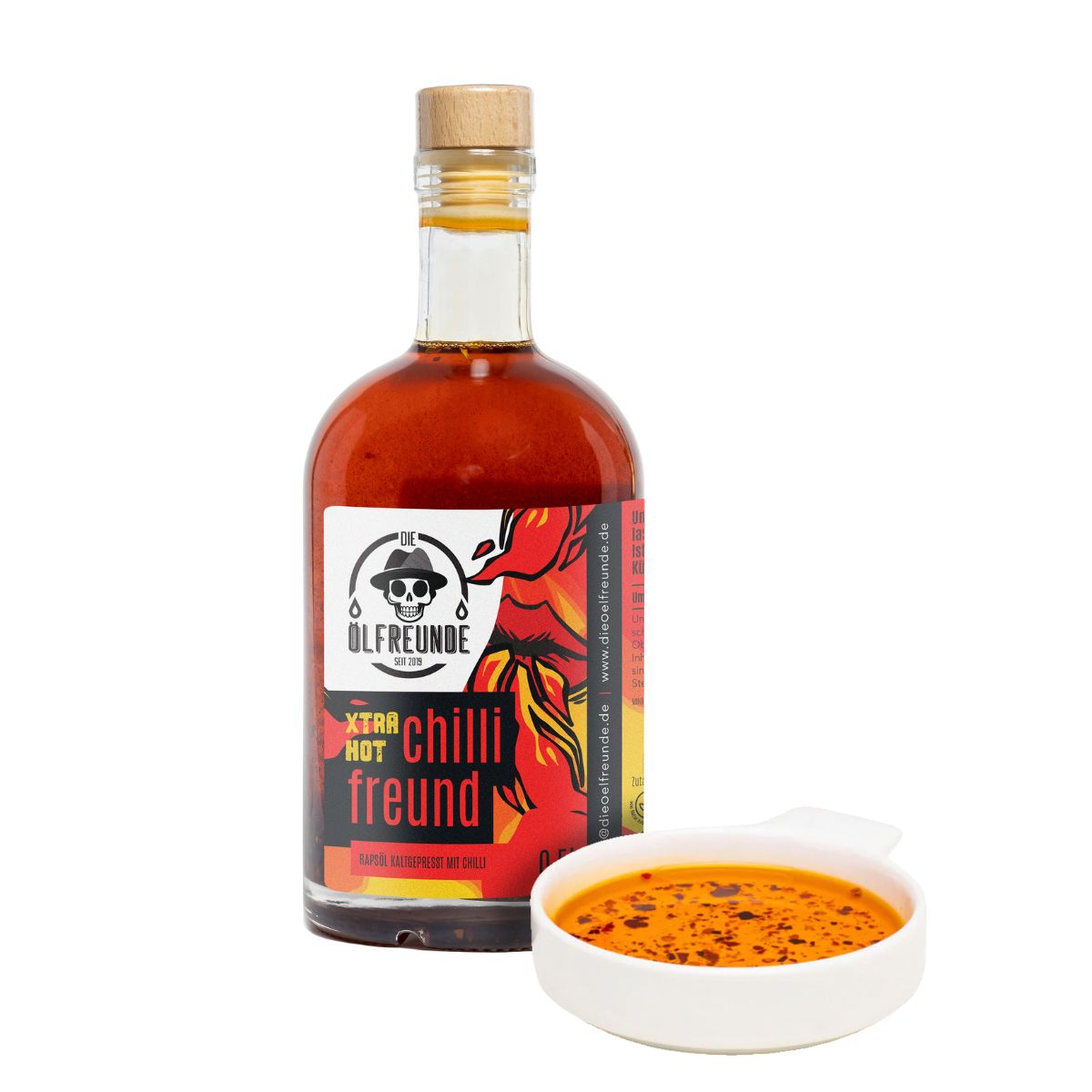 Glasflasche mit roter Flüssigkeit und Holzverschluss. Etikett: Xtra Hot Chilli Freund. Daneben eine Schale mit roter Flüssigkeit.