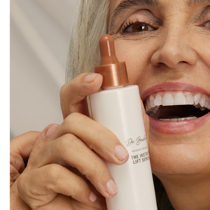 Femme tenant flacon rose avec bouchon marron. Inscription: Dr. Bouhon, THE INSTANT LIFT SERUM. Femme sourit.