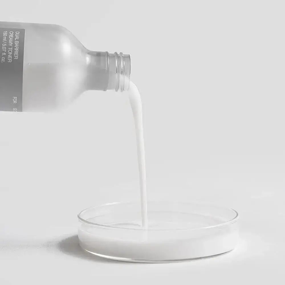 Eine Flasche gießt eine milchige Flüssigkeit in eine Petrischale. Produkt: Dual Barrier Creamy Toner.