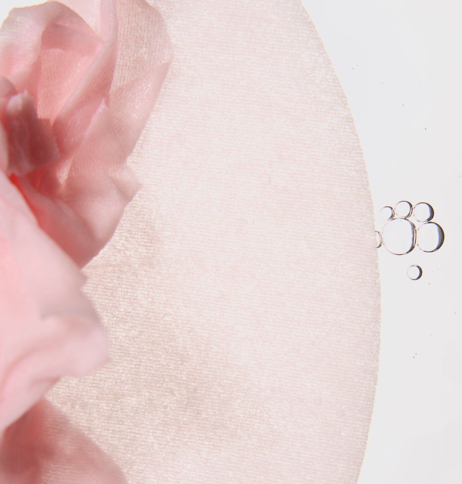 Rosa Gesichtsmaske, teilweise sichtbar. Maske liegt auf einer hellen Oberfläche. Einige Wassertropfen.