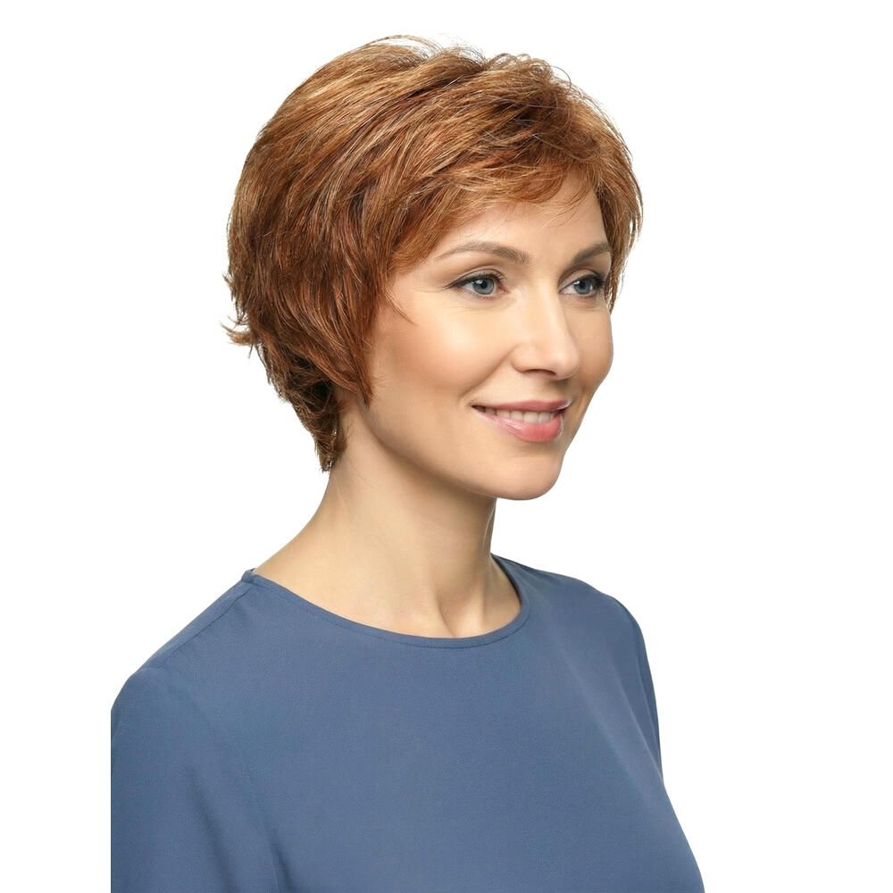 Frau mit rotbrauner Perücke, Blick zur Seite. Kurzes, gewelltes Haar. Sie trägt ein blaues Oberteil und lächelt.