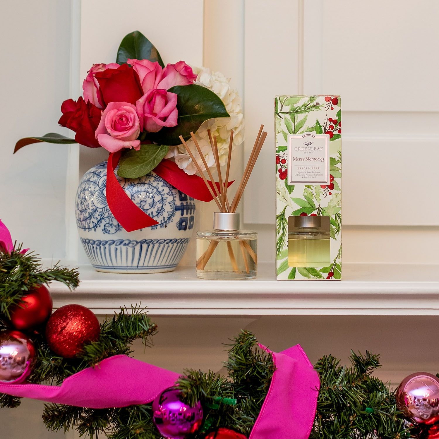 Duftspender mit Holzstäbchen neben einer Vase mit Rosen und der Produktverpackung.
