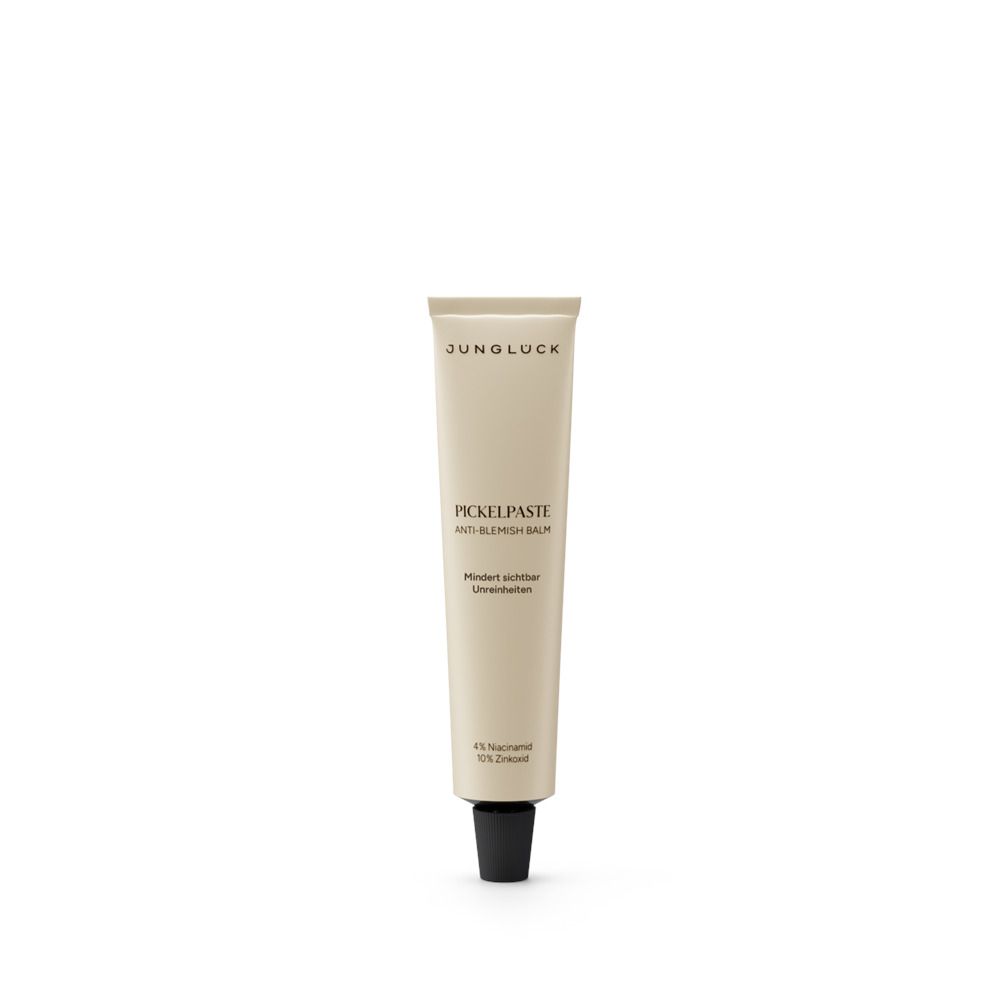 Beige Tube mit schwarzem Verschluss. Aufschrift: JUNGLÜCK, PICKELPASTE ANTI-BLEMISH BALM. Weitere Textzeilen.