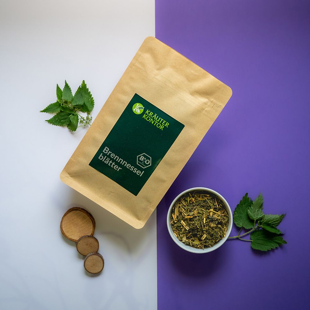 Beutel mit Brennnesselblätter-Tee, daneben Schale mit Tee, frische Blätter. Grün-braune Verpackung mit Logo und Text auf weiß-lila Hintergrund.
