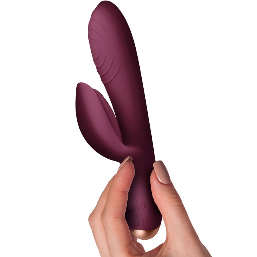Weinroter Vibrator mit Dual-Motor-Stimulation. In einer Hand gehalten. Goldfarbener Akzent am Ende.