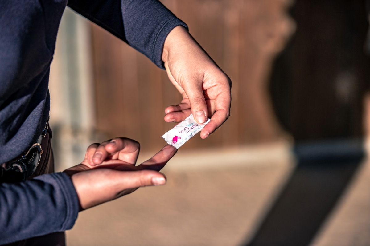 Person hält einen Stick und trägt Gel auf den Finger auf. Der Stick ist mit Produktinformationen bedruckt.