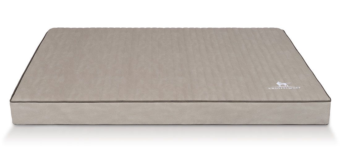 Rechteckige, beige Hundematte mit schwarzem Rand. Das Logo ist rechts unten sichtbar. Die Oberfläche ist gesteppt.