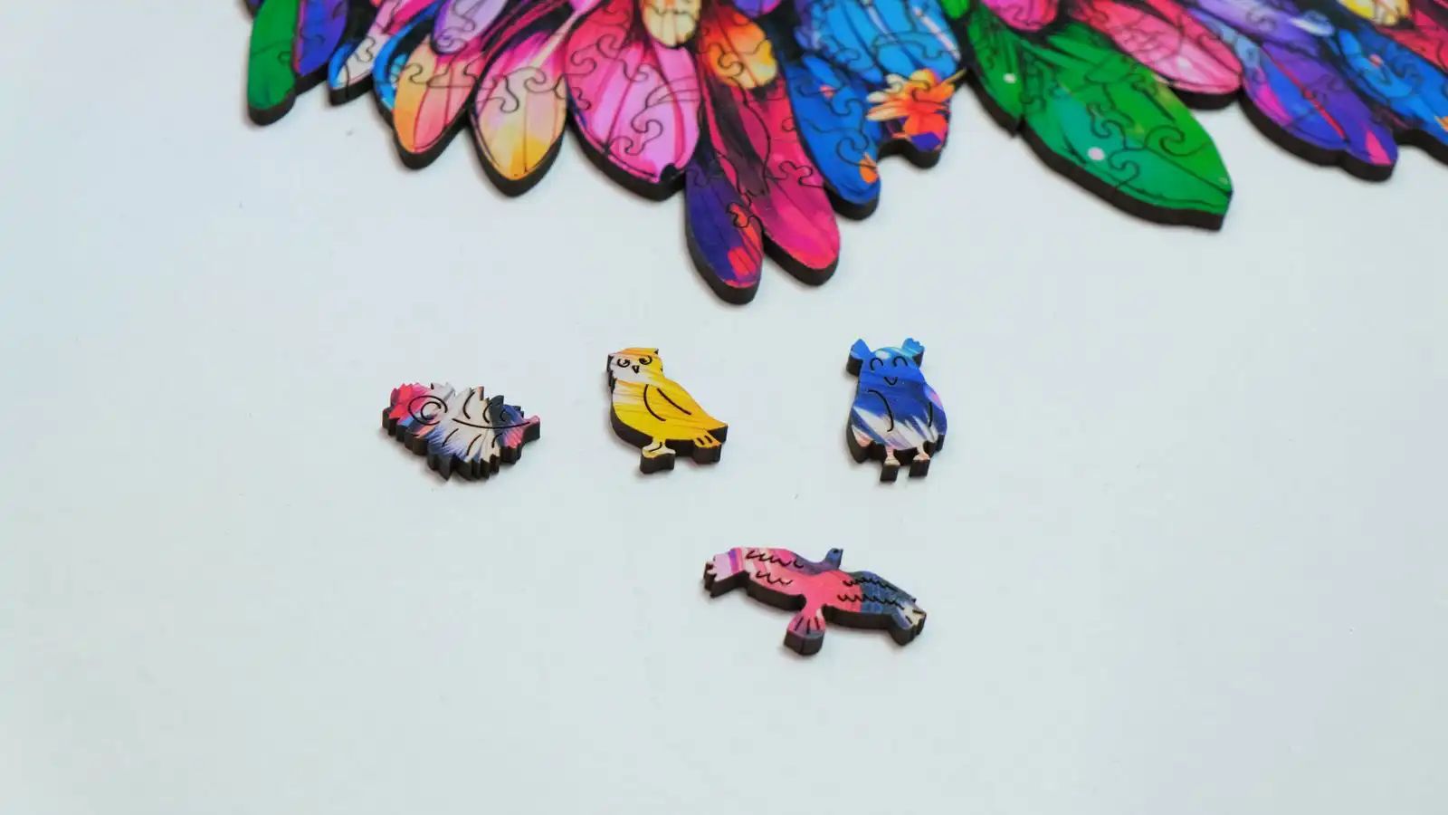Nahaufnahme von Puzzleteilen mit Eulenmotiven. Verschiedene Formen und Farben. Einzelne Puzzleteile liegen auf weißem Hintergrund.