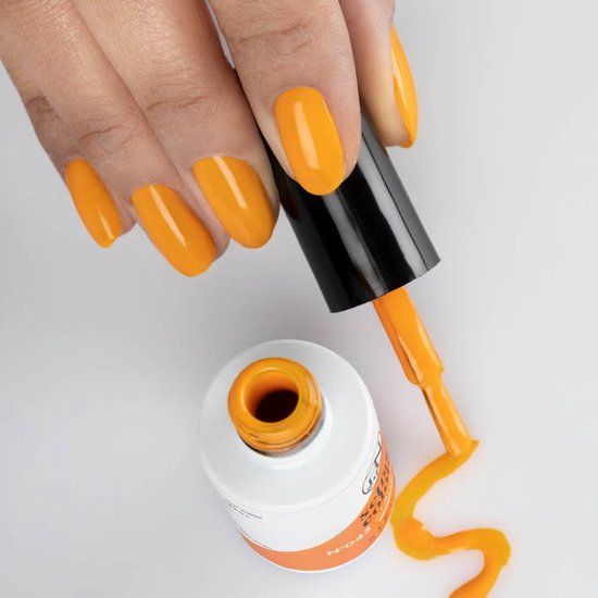 Hand mit orangefarben lackierten Nägeln. Nagellackflasche und Pinsel daneben. Lack auf der Oberfläche.