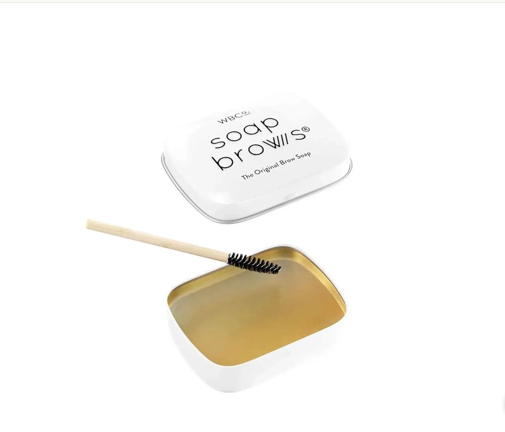 Weißes, quadratisches Döschen mit Schriftzug. Darunter ein offenes Döschen mit Bürste.