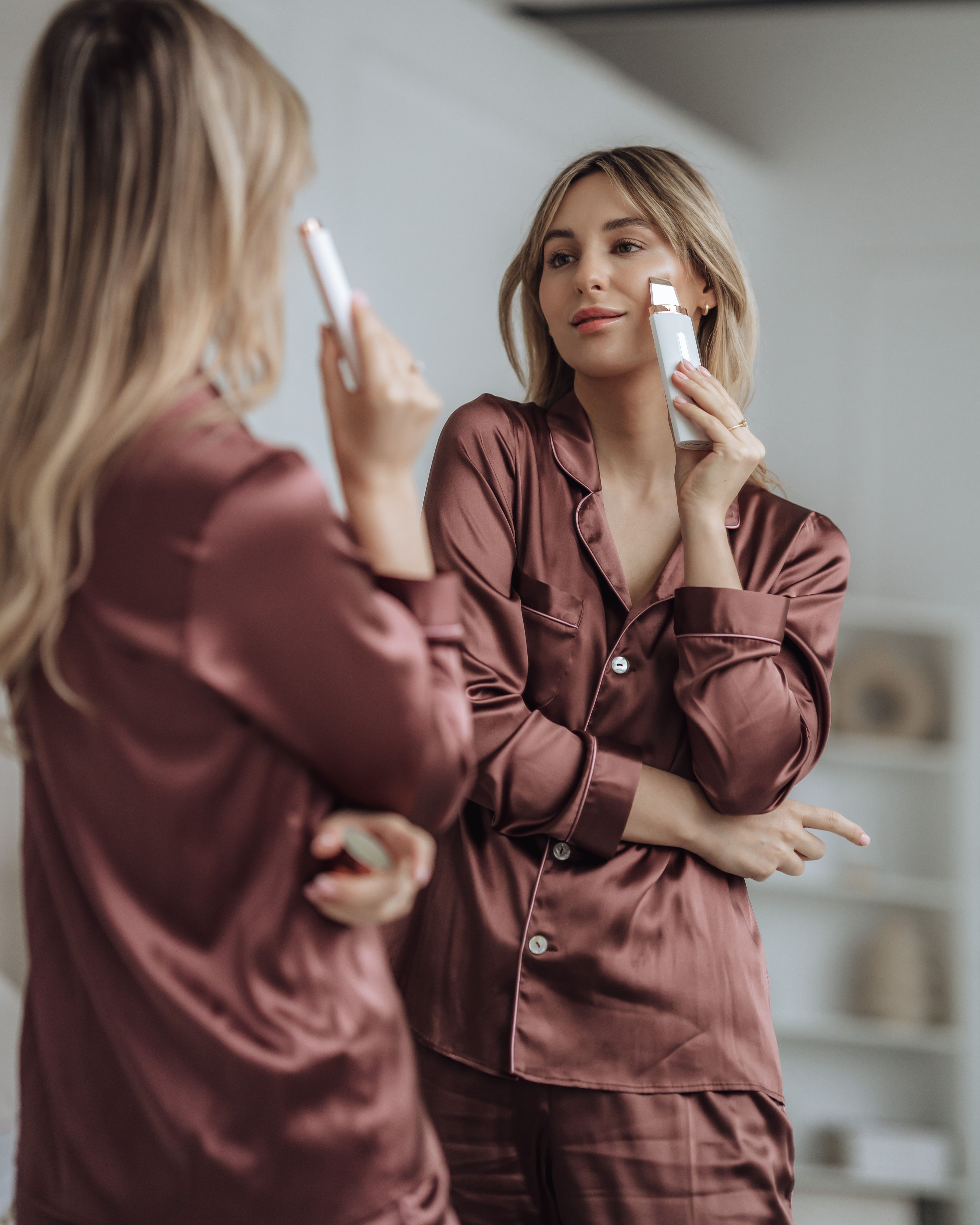 Frau im Spiegel, hält ein weißes BEAUTIFLY B-Scrub Pro Slim Ultraschall Peeling. Sie berührt ihr Gesicht.
