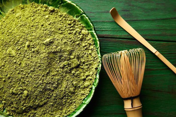 Grünes Matcha-Pulver in einer Schale, daneben ein Bambusbesen und ein Löffel.