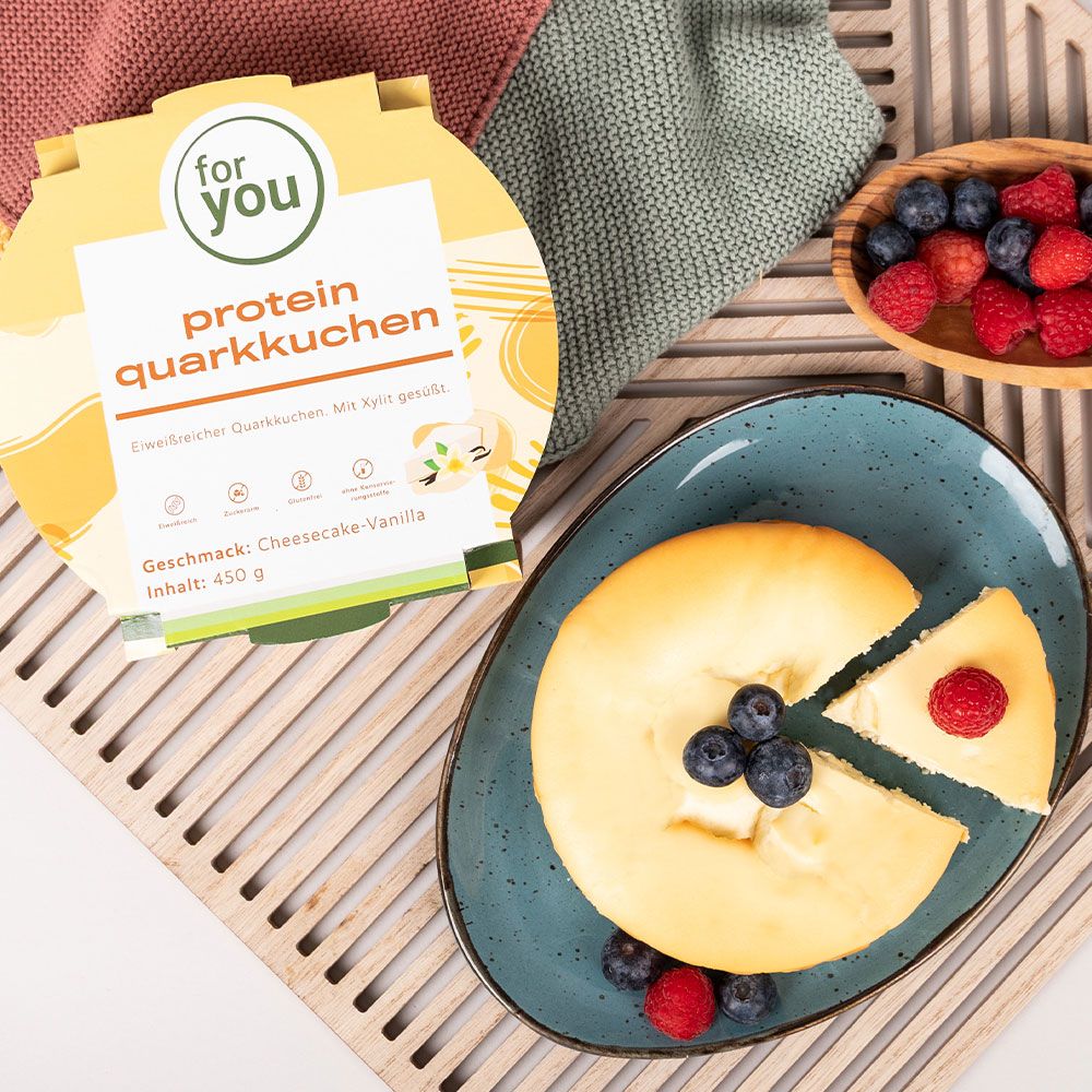 Quarkkuchen auf einem blauen Teller, daneben die Verpackung. Blaubeeren und Himbeeren als Dekoration.