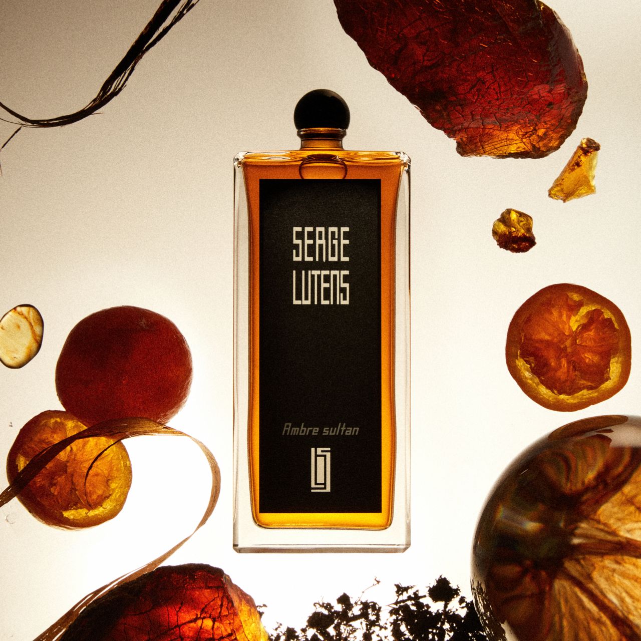 Rechteckiger Flakon mit schwarzem Etikett. Auf dem Etikett steht "SERGE LUTENS Ambre sultan". Der Flakon ist von Dekoration umgeben.