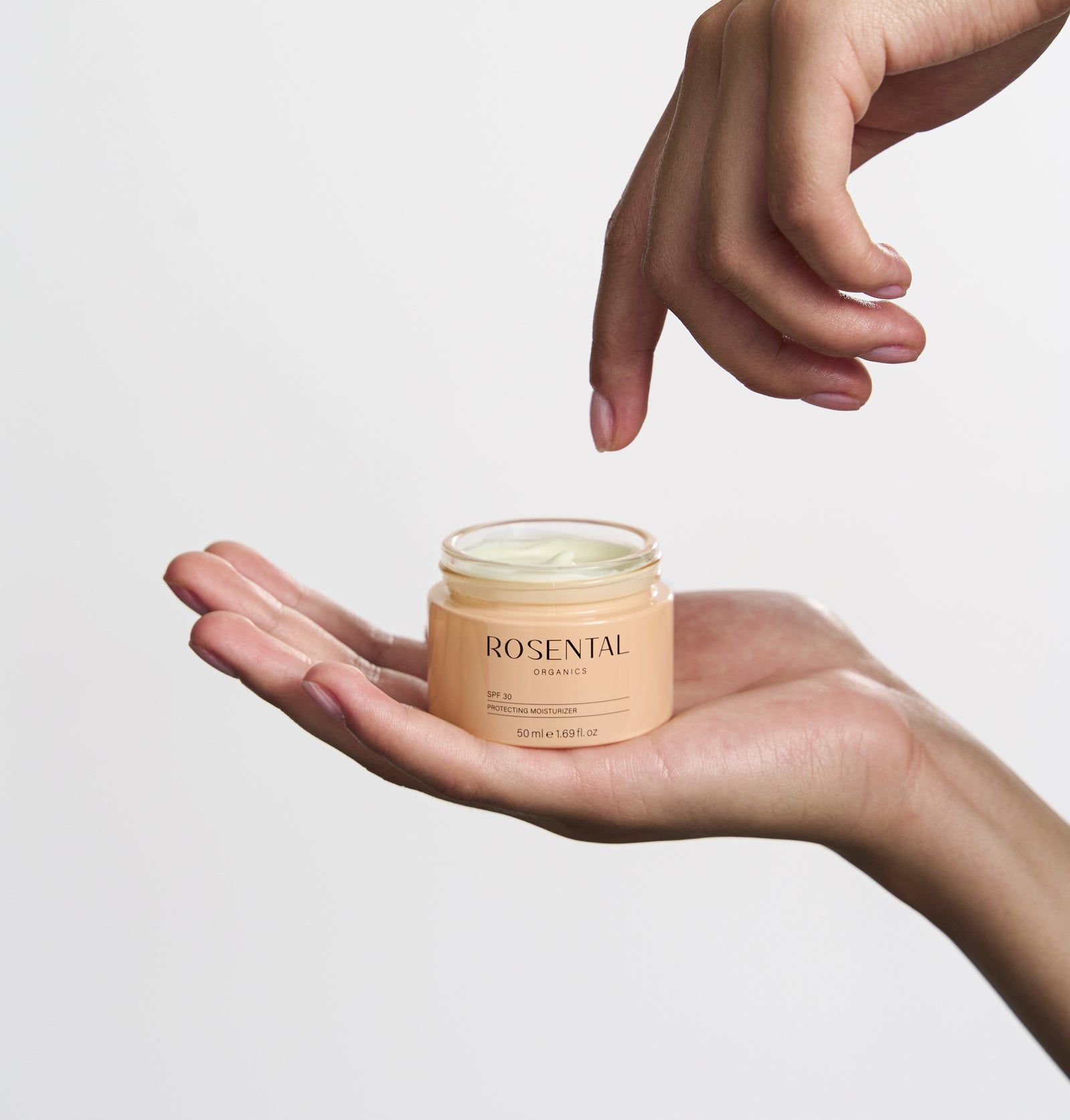 Hände halten eine Creme-Dose. Auf der Dose steht SPF 30. Die Dose ist hellbraun.