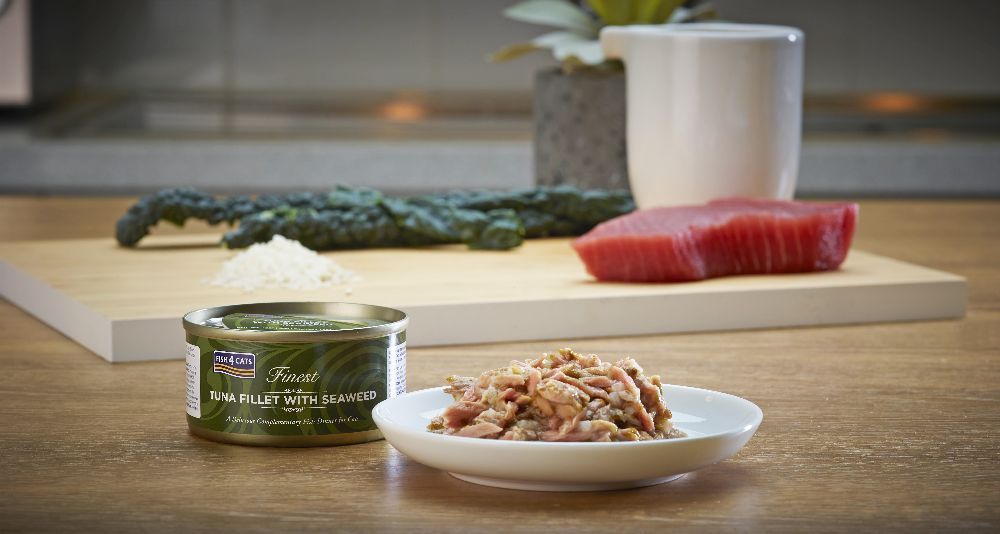 Eine Dose Thunfischfilet mit Seealgen neben einer kleinen Schale mit Futter. Auf einem Brett sind Zutaten drapiert.