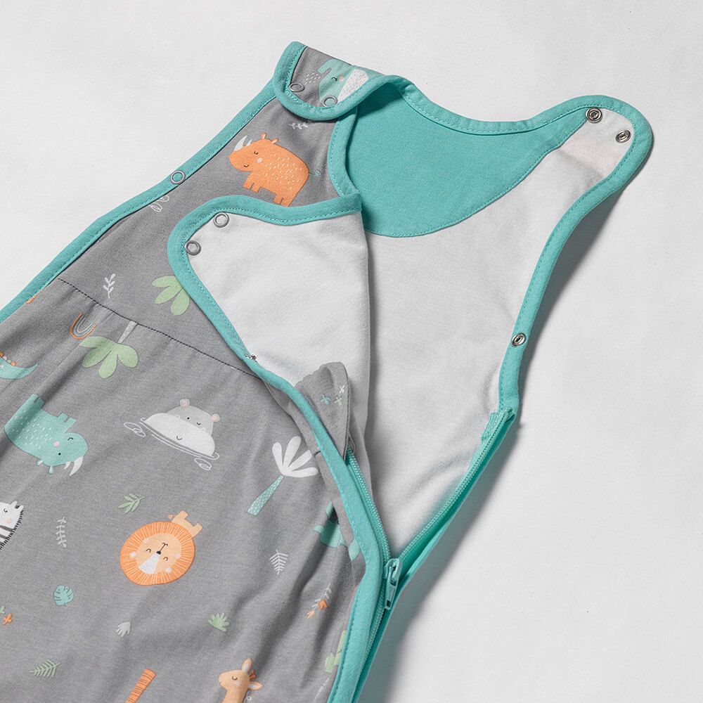 Nahaufnahme eines grauen Babyschlafsacks mit Safari-Muster. Türkisfarbene Einfassung. Reißverschluss und Druckknöpfe.