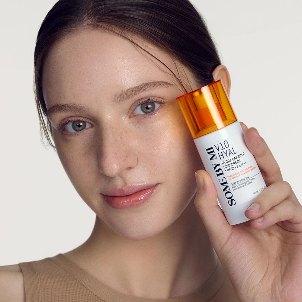 Frau hält Flakon. Aufschrift: V10 Hyal Hydra Capsule Sunscreen SPF50+ PA++++. Flakon mit orangefarbenem Deckel. Gesicht der Frau im Vordergrund.