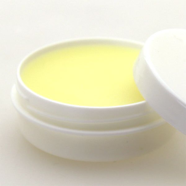 Vasetto bianco aperto con balsamo per labbra giallo. Coperchio accanto.