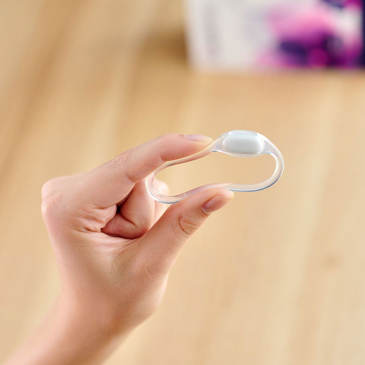 Hand hält OvulaRing. Transparenter Ring mit weißem Sensor.