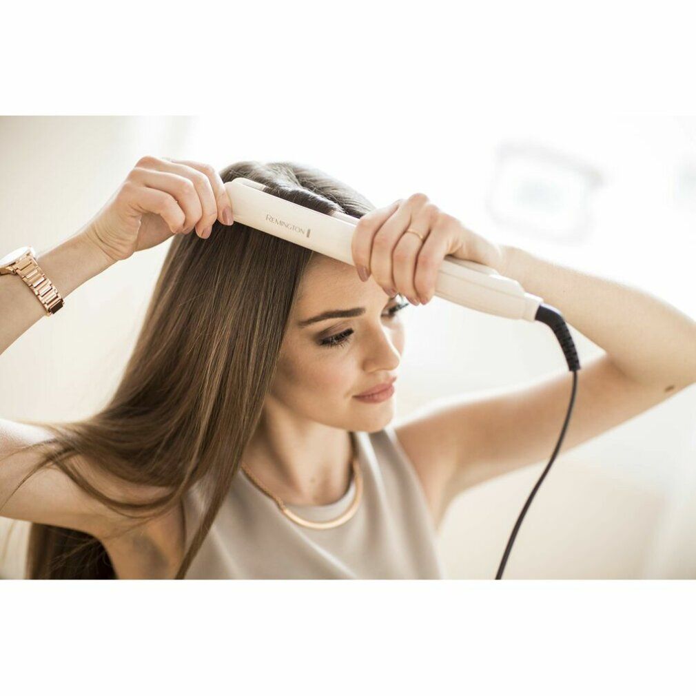 Frau benutzt Haarglätter. Beige Haarglätter. Marke Remington. Goldene Uhr und Halskette.