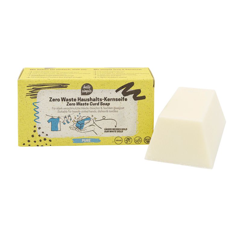 Ein Stück helle Kernseife neben einer gelben Schachtel. Auf der Schachtel steht "hello simple Zero Waste Haushalts-Kernseife".