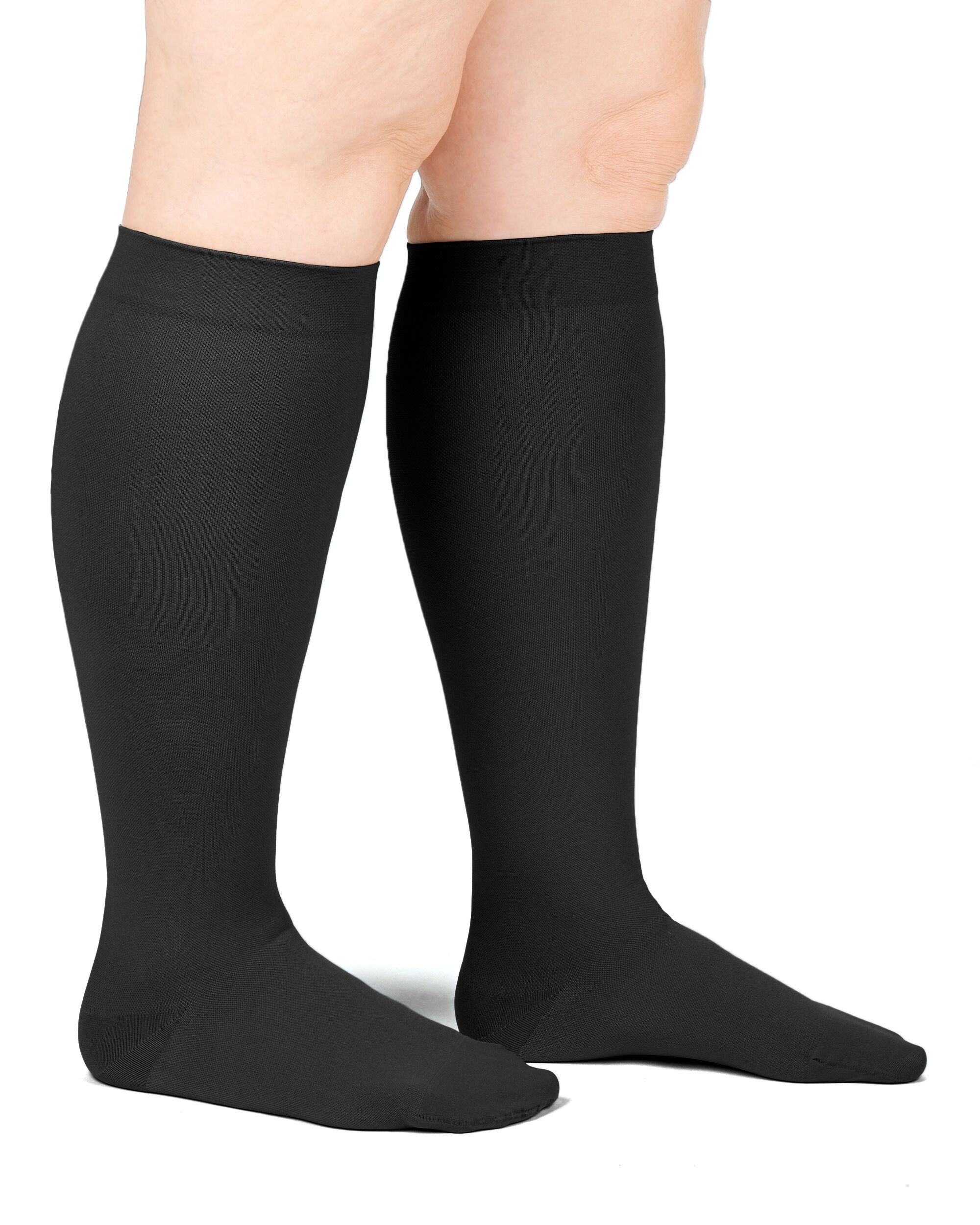 Zwei schwarze Kompressions-Kniestrümpfe an Beinen. Blick von der Seite. Glattes Material, ohne sichtbare Muster.