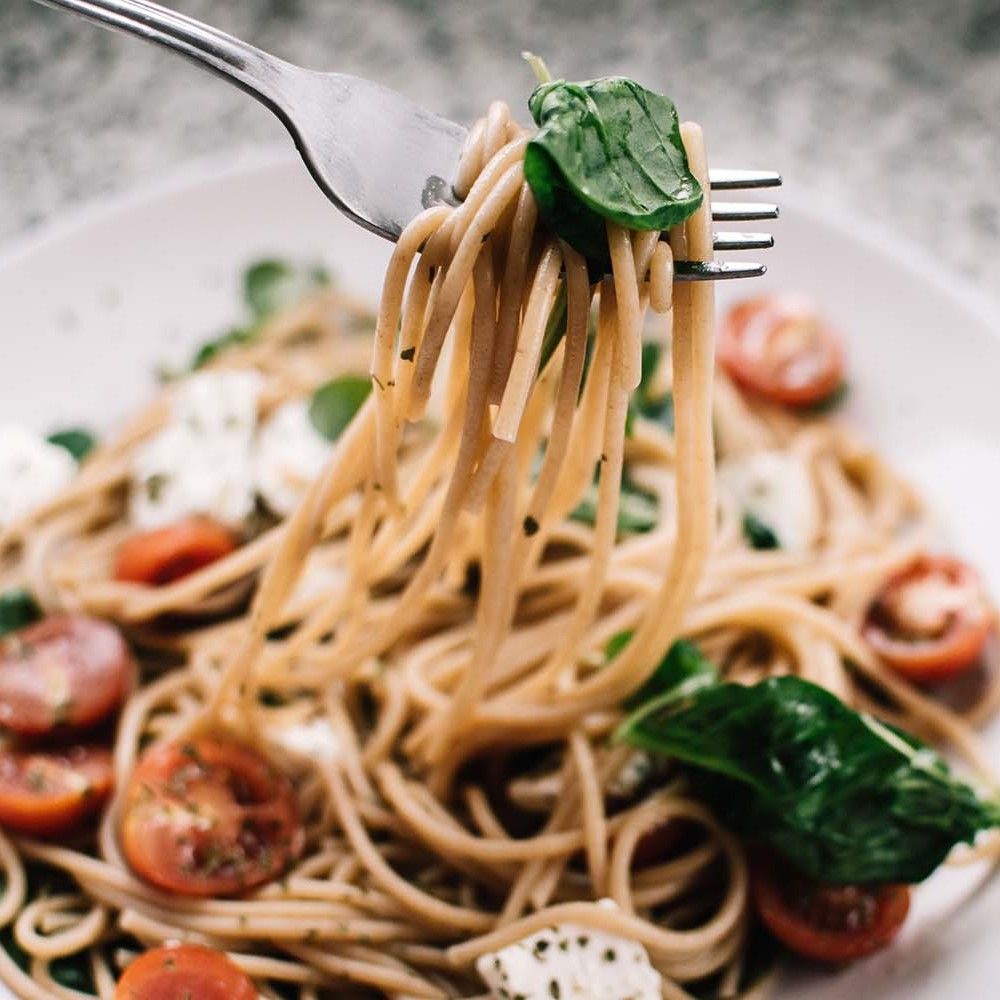 Spaghetti mit Tomaten, Mozzarella und Basilikum, auf einer Gabel. Teller mit Pasta.