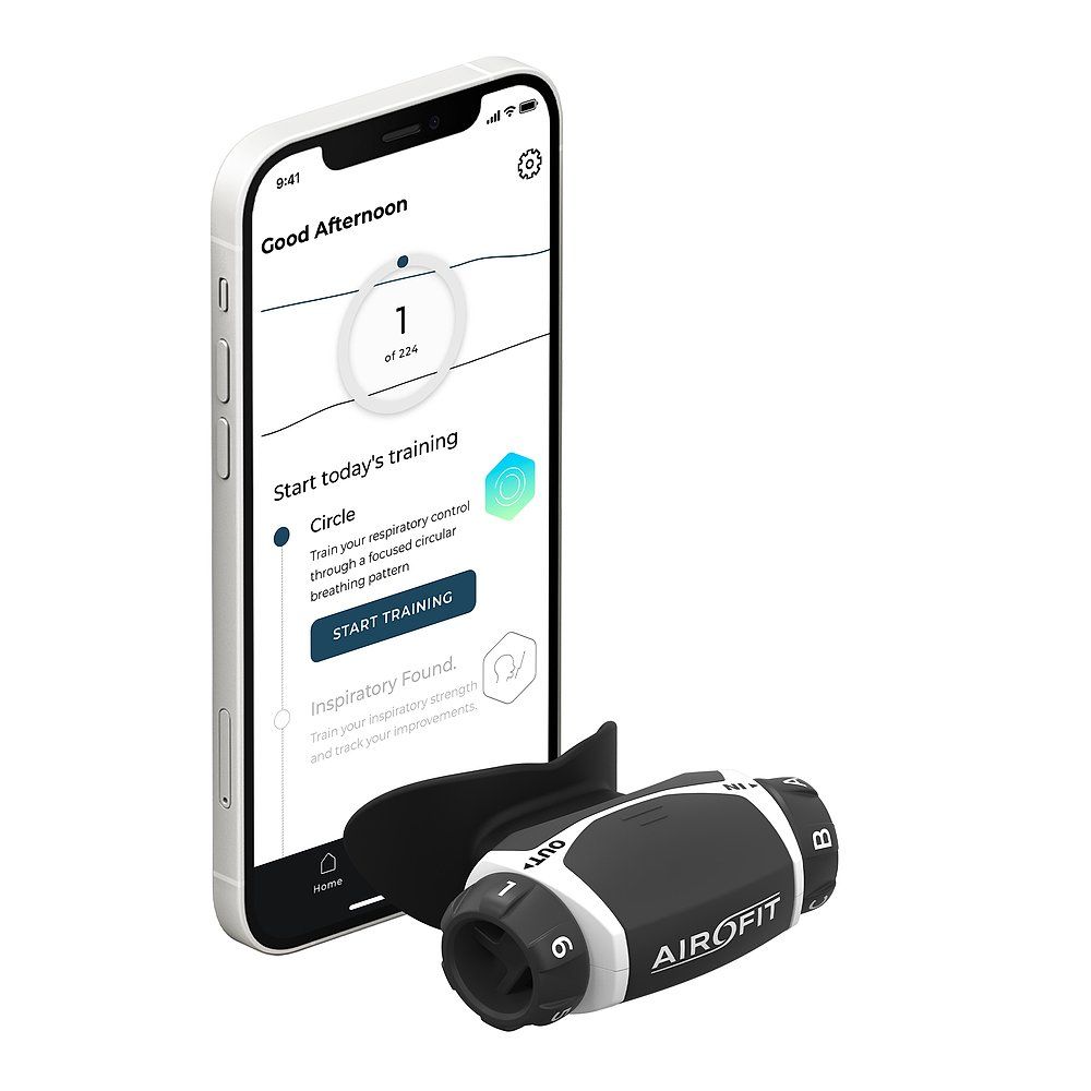 Atemtrainer neben Smartphone mit App-Anzeige. Schwarzes Gerät mit weißer Beschriftung. App zeigt Trainingsdaten.