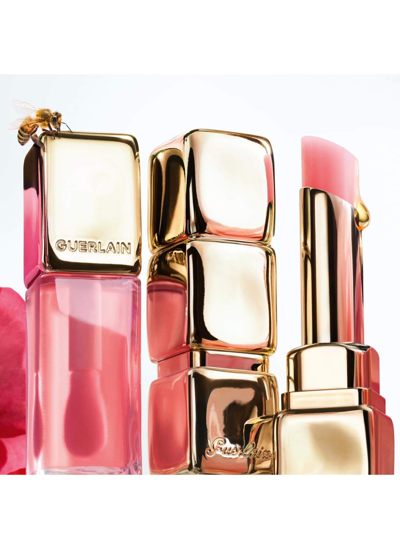 Mehrere Lippenbalsam-Stifte, rosa Hüllen mit goldenen Details. Eine Biene sitzt auf einem Stift. Honigtropfen fließen.