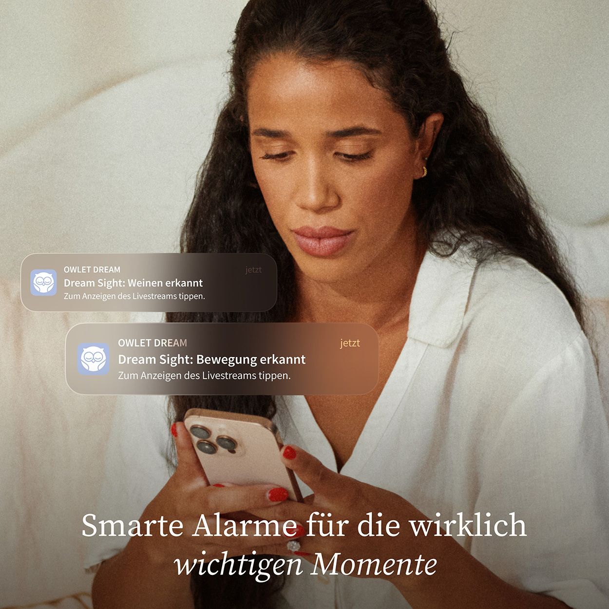 Frau hält Smartphone mit Owlet Dream Sight-Alarmmeldungen. Benachrichtigungen über Bewegung und Weinen.