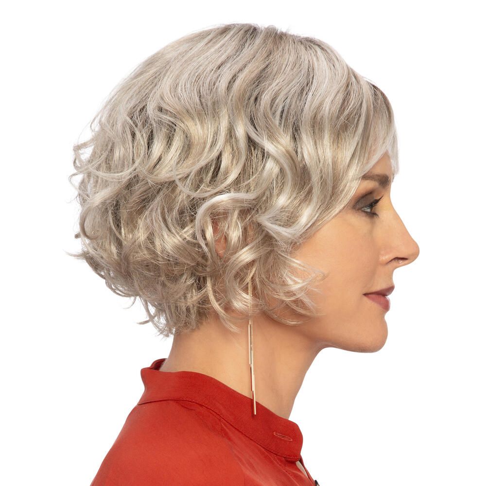 Perücke Biarritz von DELUXE. Blond gewellt, mit Pony. Frau mit roter Bluse. Profilansicht.